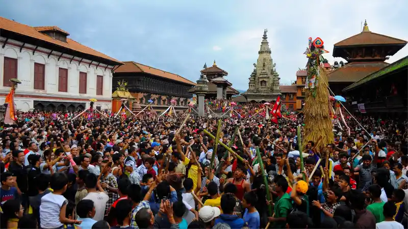 Crowd at a vibrant Nepal cultural festival, possibly Gai Jatra, with traditional architecture in the background.