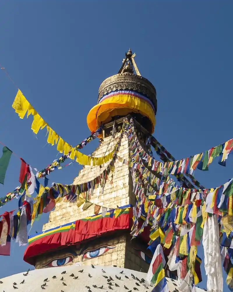 Colorful prayer flags decorate a temple spire against a clear blue sky in Nepal.